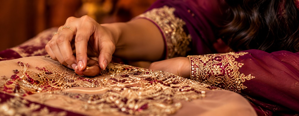 Hands working on intricate gold embroidery and jeweled details
